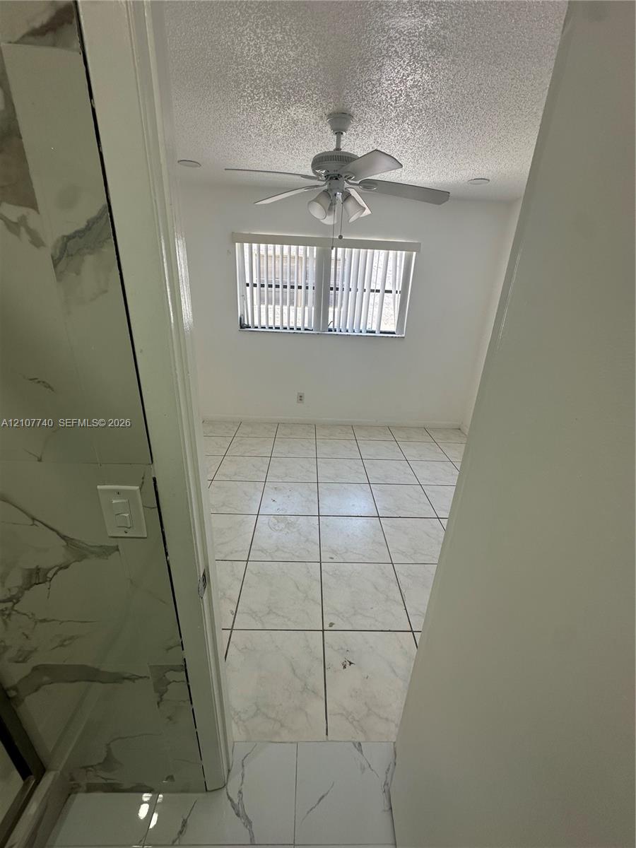 Large-format tile flooring, ceiling fan with integrated lighting, and vertical window blinds