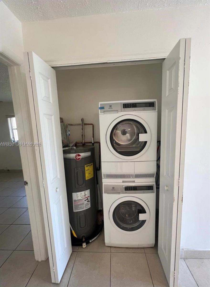 Utility closet featuring a stacked front-loading washer and dryer unit and a vertical water heater