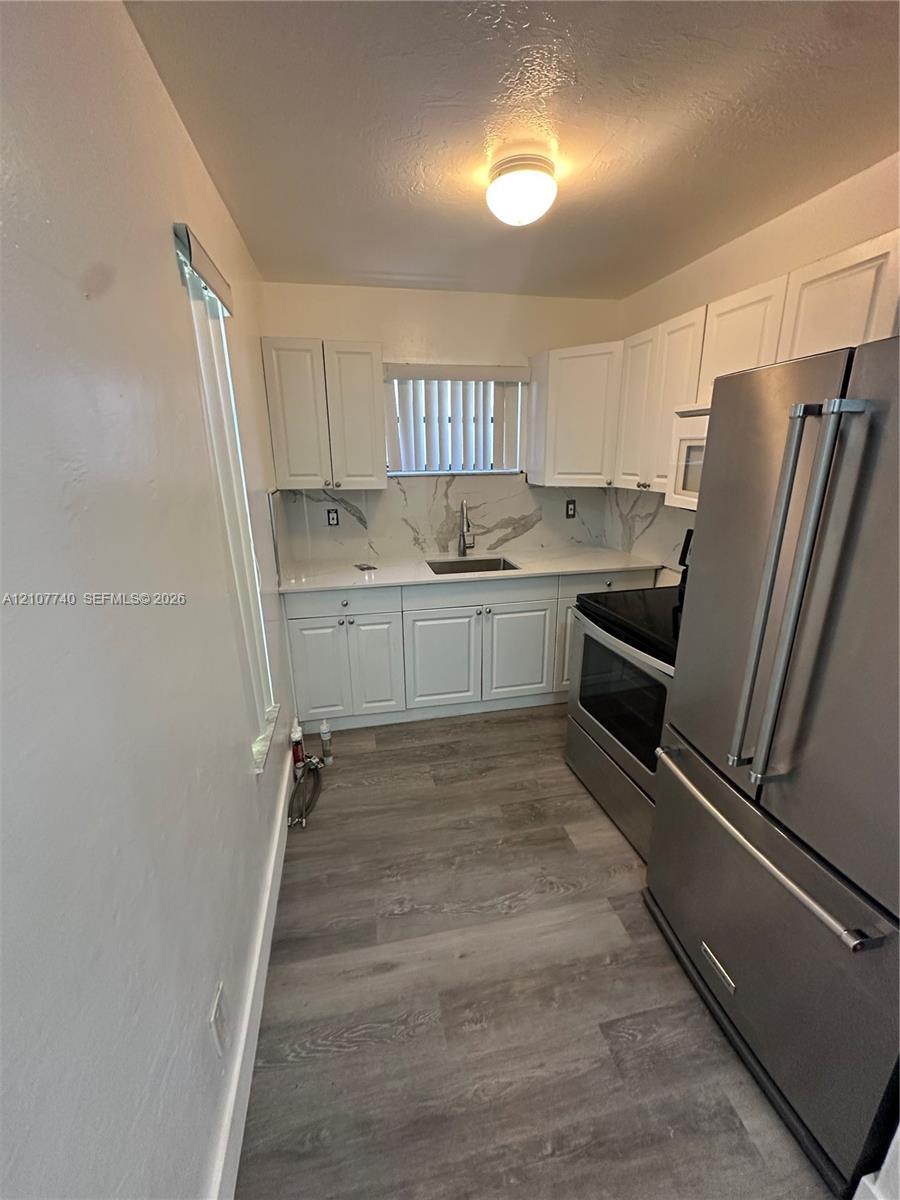 Kitchen featuring white cabinetry, stone-surface countertops with a decorative backsplash, stainless steel appliances, and wood-finish flooring