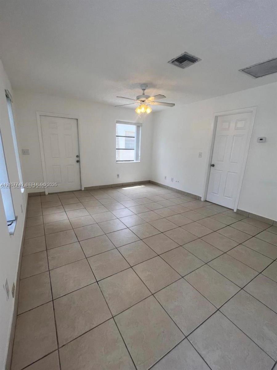 Interior space featuring large-format ceramic tile flooring, neutral walls, a multi-blade ceiling fan with integrated lighting, and solid-core interior doors
