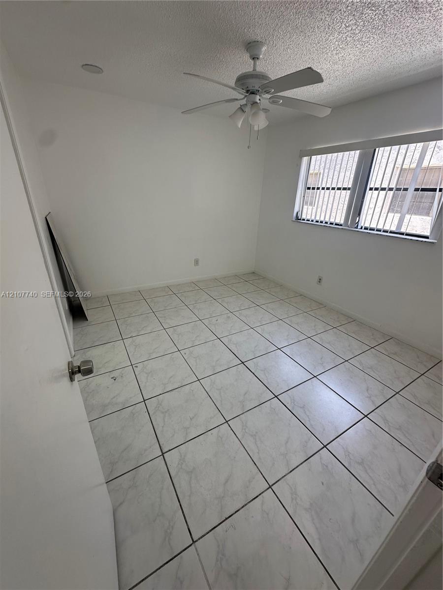 Room featuring large-format stone-patterned tile flooring, a multi-blade ceiling fan with integrated lighting, and a window with horizontal blinds