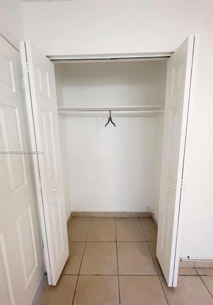 Storage closet featuring dual bifold doors, a built-in shelf, a hanging rod, and ceramic tile flooring