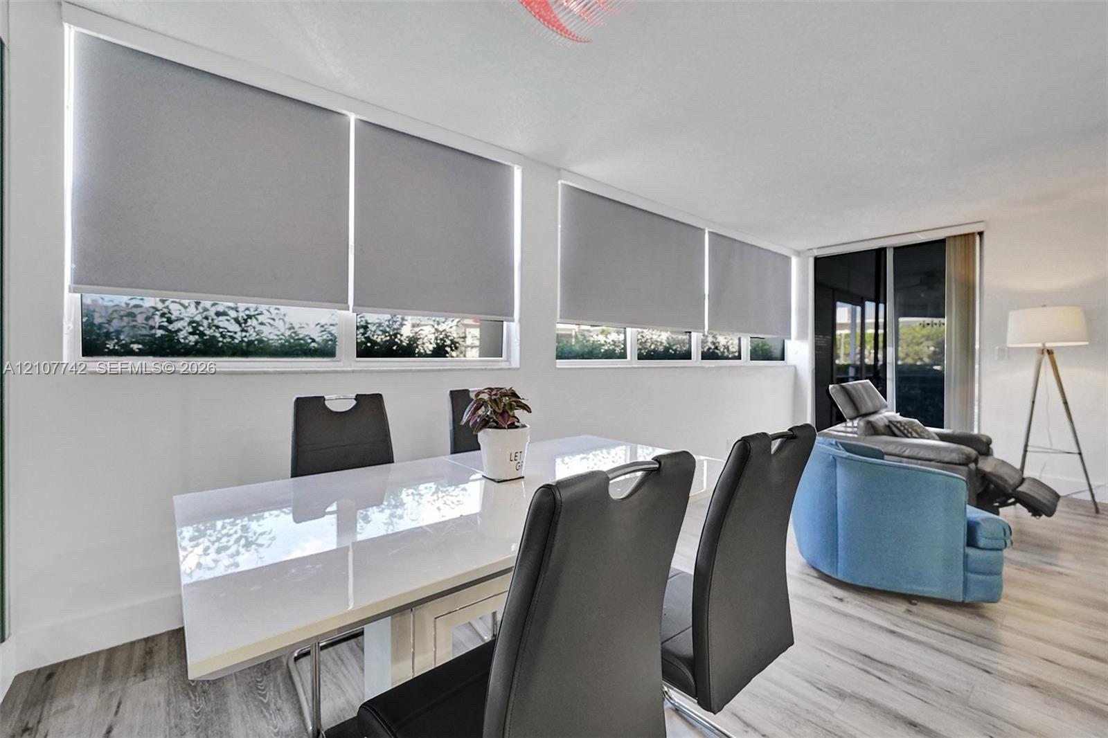 Sun-filled interior featuring expansive picture windows, custom roller shades, sliding glass door, and wood-finish flooring