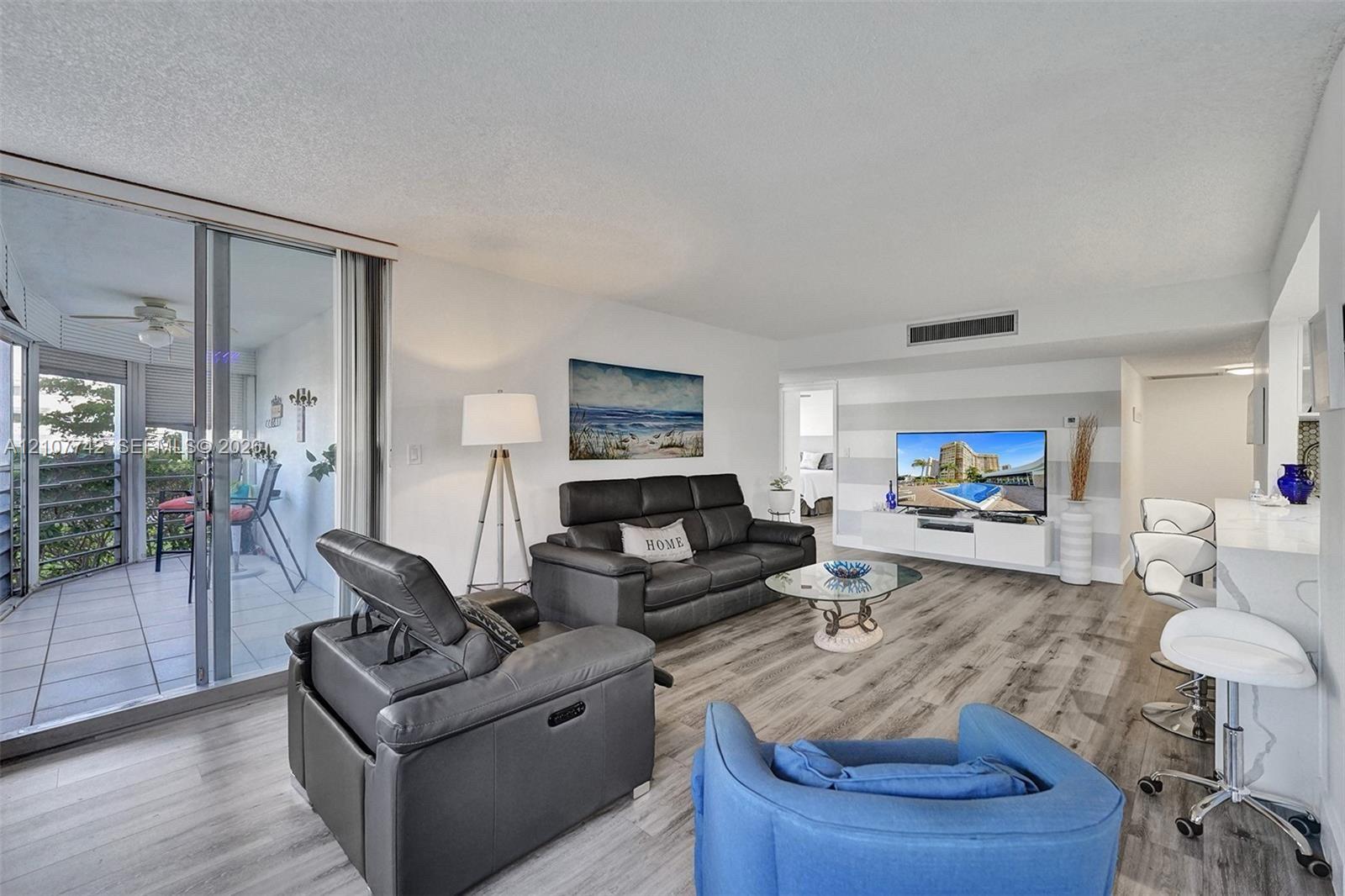 Living area featuring wood-finish flooring, a built-in media console, a breakfast bar with stone-finish countertop, and floor-to-ceiling glass sliding doors opening to a private balcony