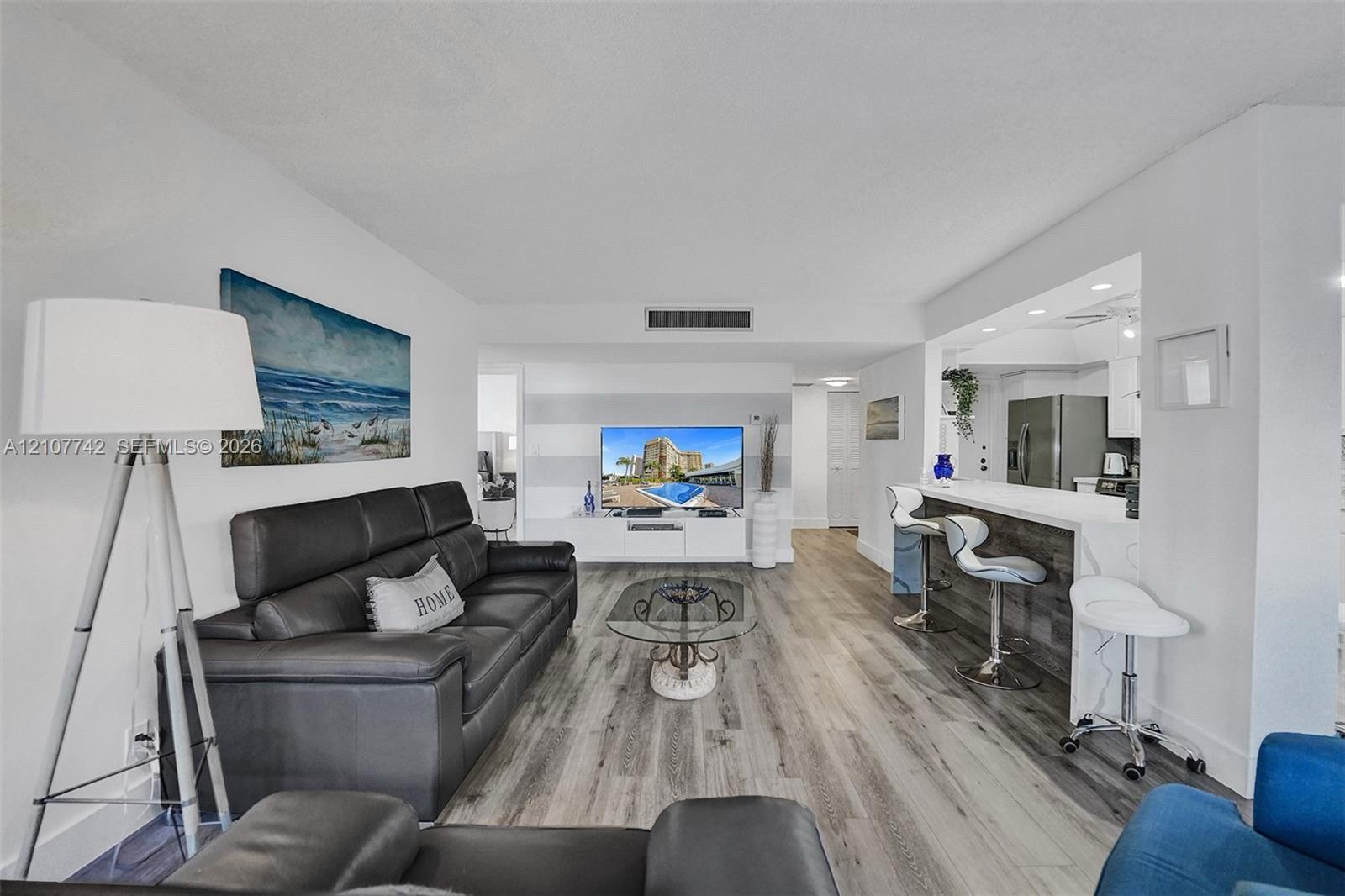 Open-concept living space featuring wood-finish flooring, recessed lighting, and a breakfast bar with a stone-finish facade