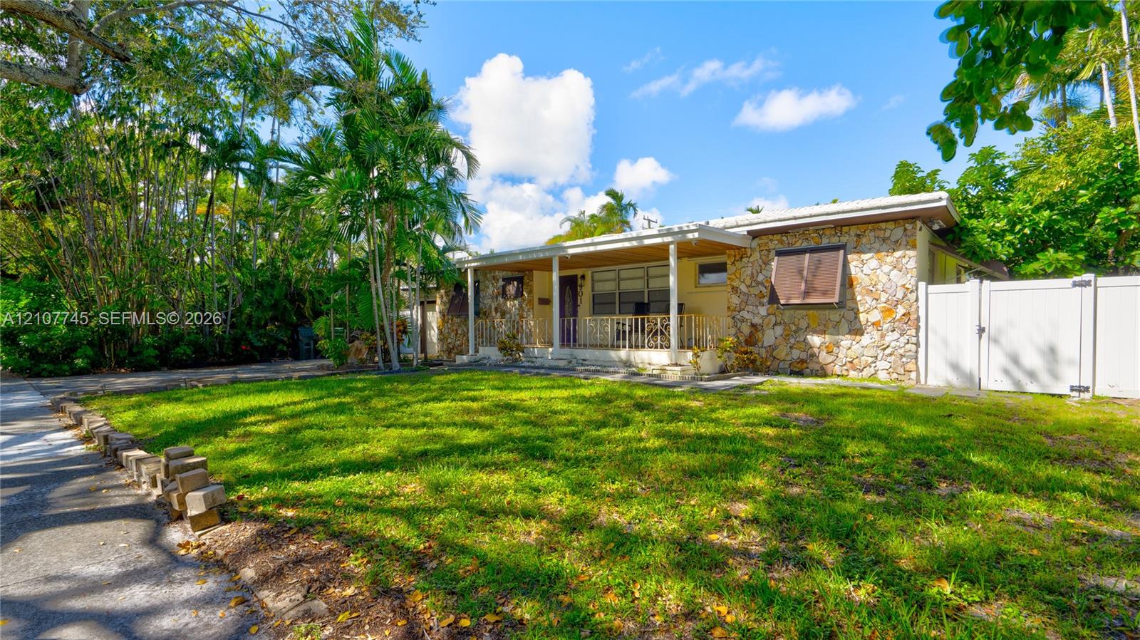 Single-story exterior featuring natural stone veneer, a covered front porch, and a white privacy fence