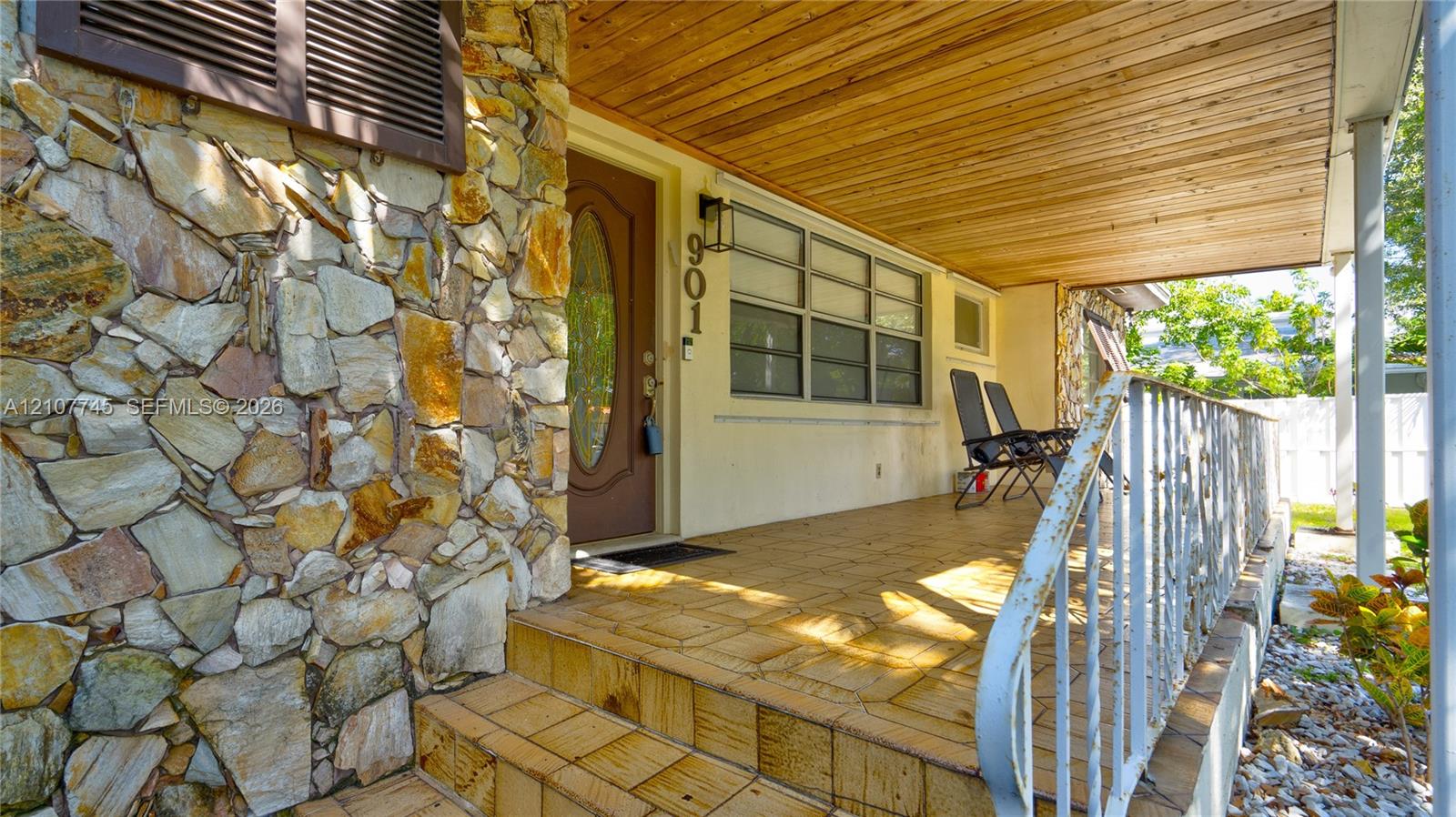 Covered porch featuring a wood-plank ceiling, natural stone facade, tiled flooring, and decorative metal railing