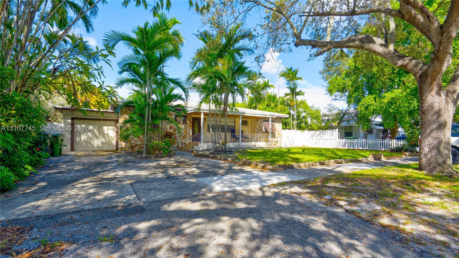 Single-story residence featuring a concrete driveway, attached one-car garage, covered front porch, and white picket fencing