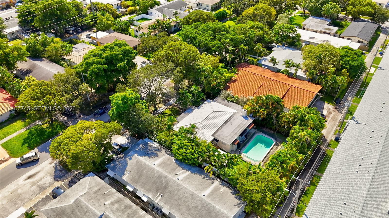 Aerial view featuring a light-toned hip roof, an inground swimming pool, and mature landscaping