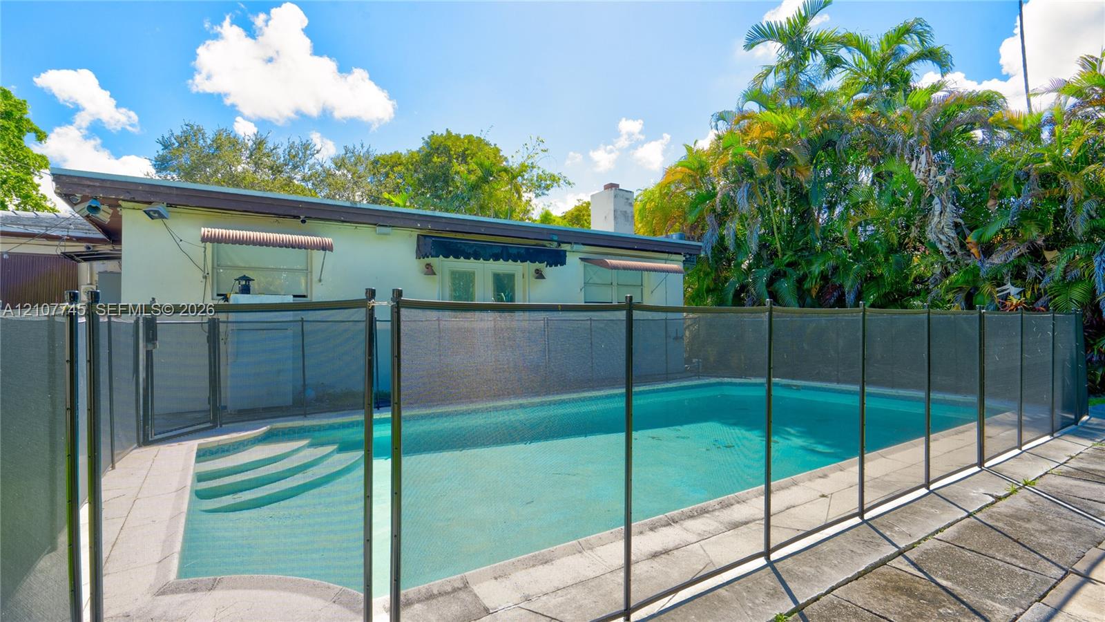In-ground pool featuring a removable mesh safety fence and a concrete pool deck