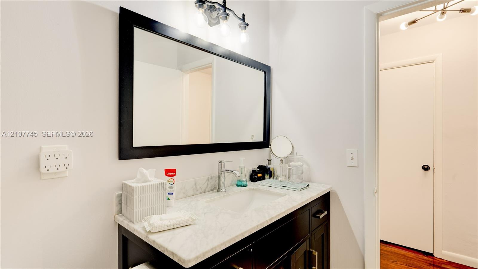 Vanity featuring a stone countertop, integrated sink, dark wood-finish cabinetry, a large framed mirror, and a multi-bulb light fixture