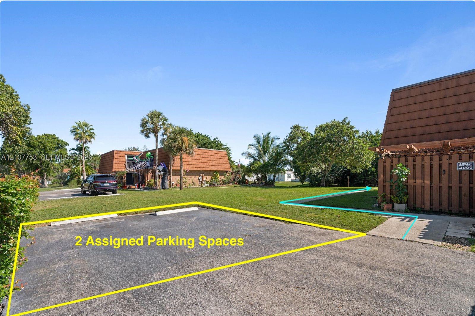Two assigned parking spaces featuring asphalt paving, set within an exterior grounds area with mature palm trees and green space