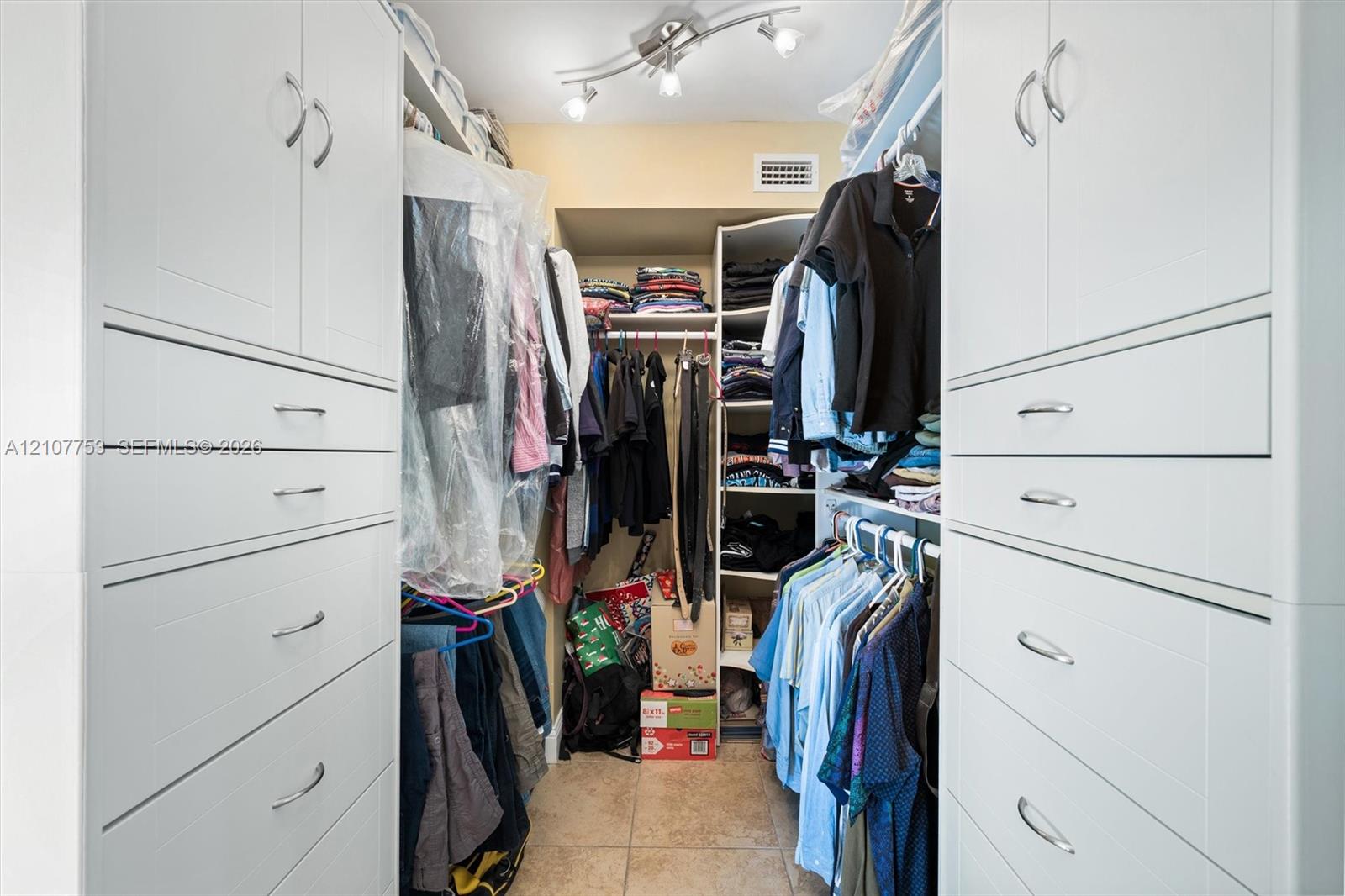 Walk-in closet featuring extensive built-in white cabinetry, multi-tiered shelving, drawer storage, chrome hardware, and overhead track lighting
