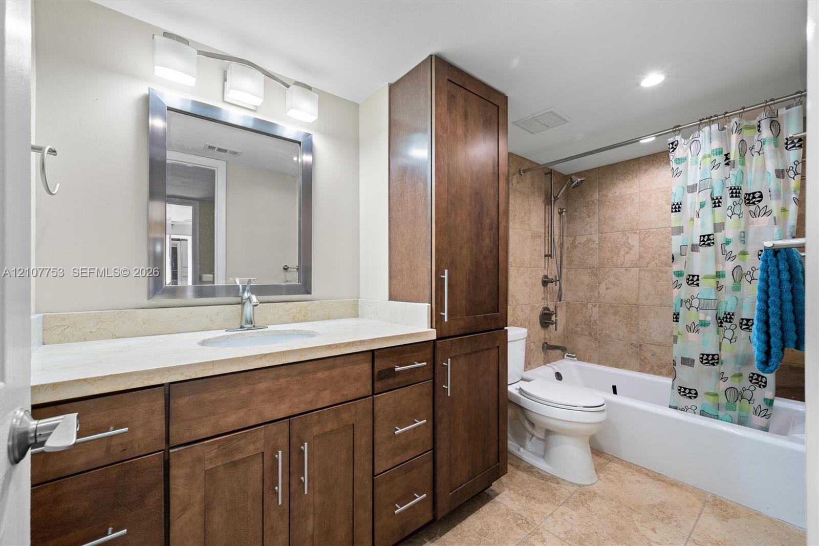Bathroom featuring a vanity with dark wood-finish cabinetry, stone-composite countertop, full-height built-in linen tower, metallic wall-mounted vanity lighting, and a tub-shower combination with floor-to-ceiling tile surround