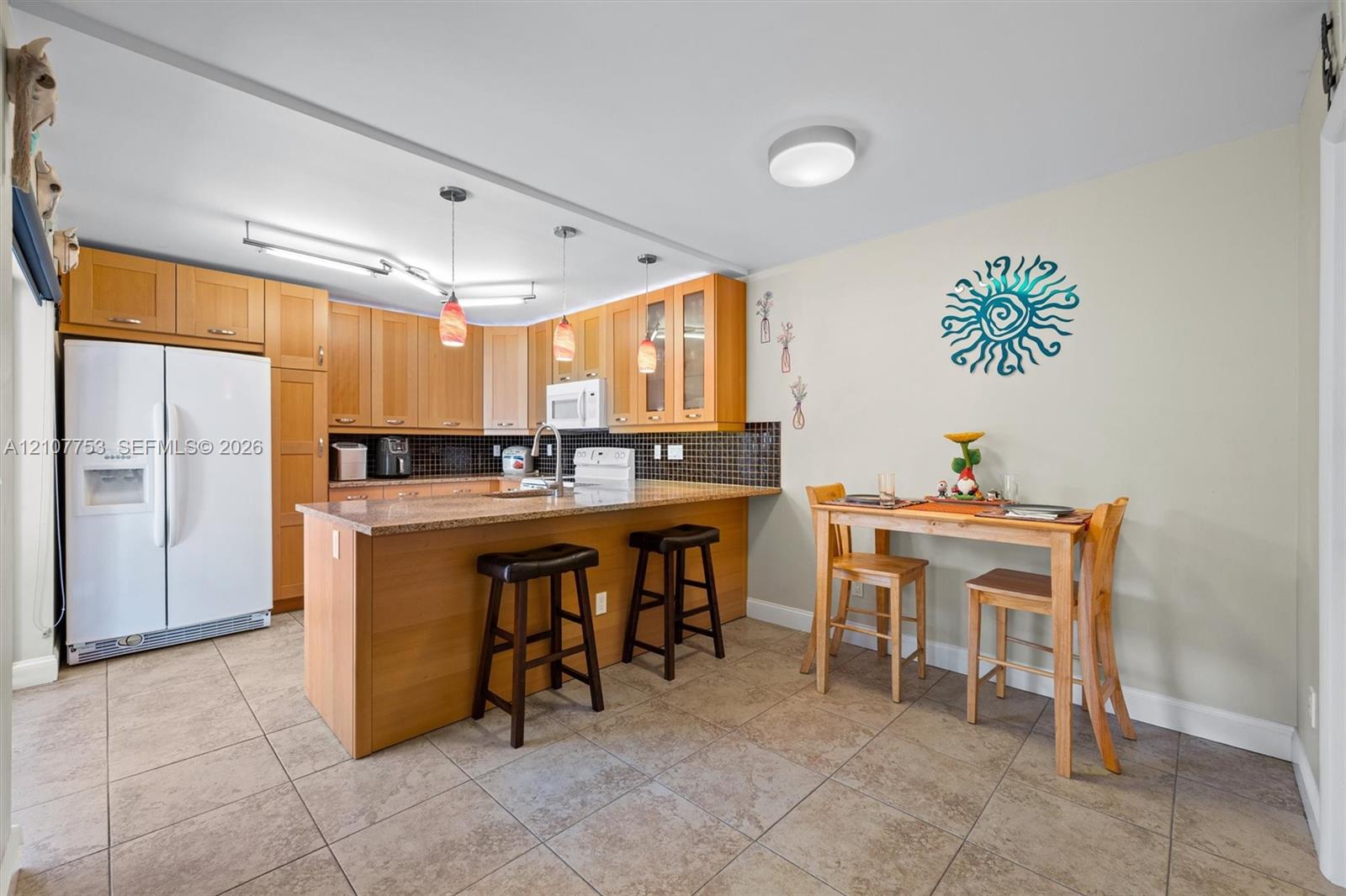 Kitchen featuring wood cabinetry, stone-finish countertops, tiled backsplash, center island with breakfast bar seating, and tile flooring