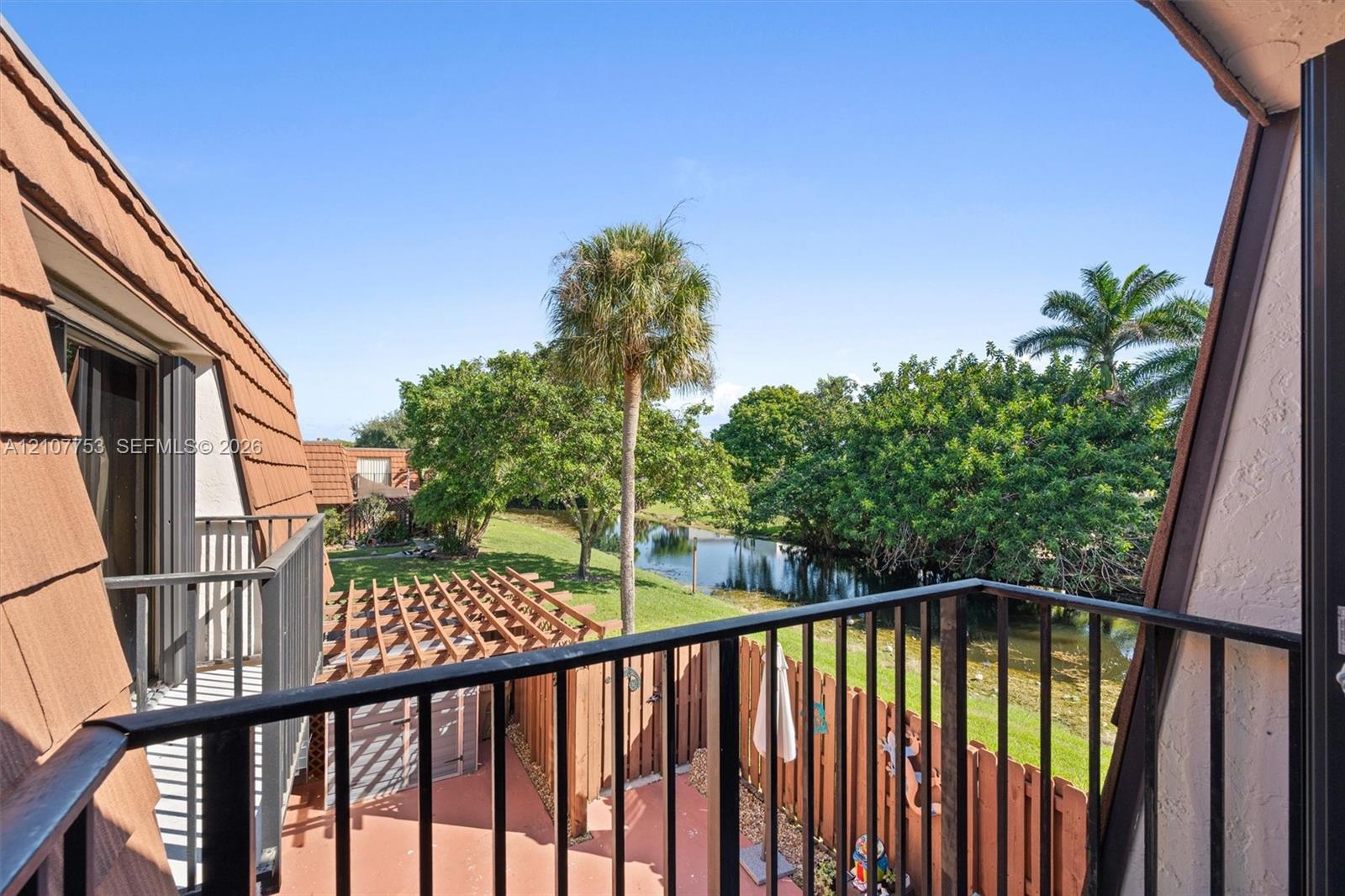 Private balcony with metal railing, clay-tile roofing, cedar-tone wooden pergola, and water frontage