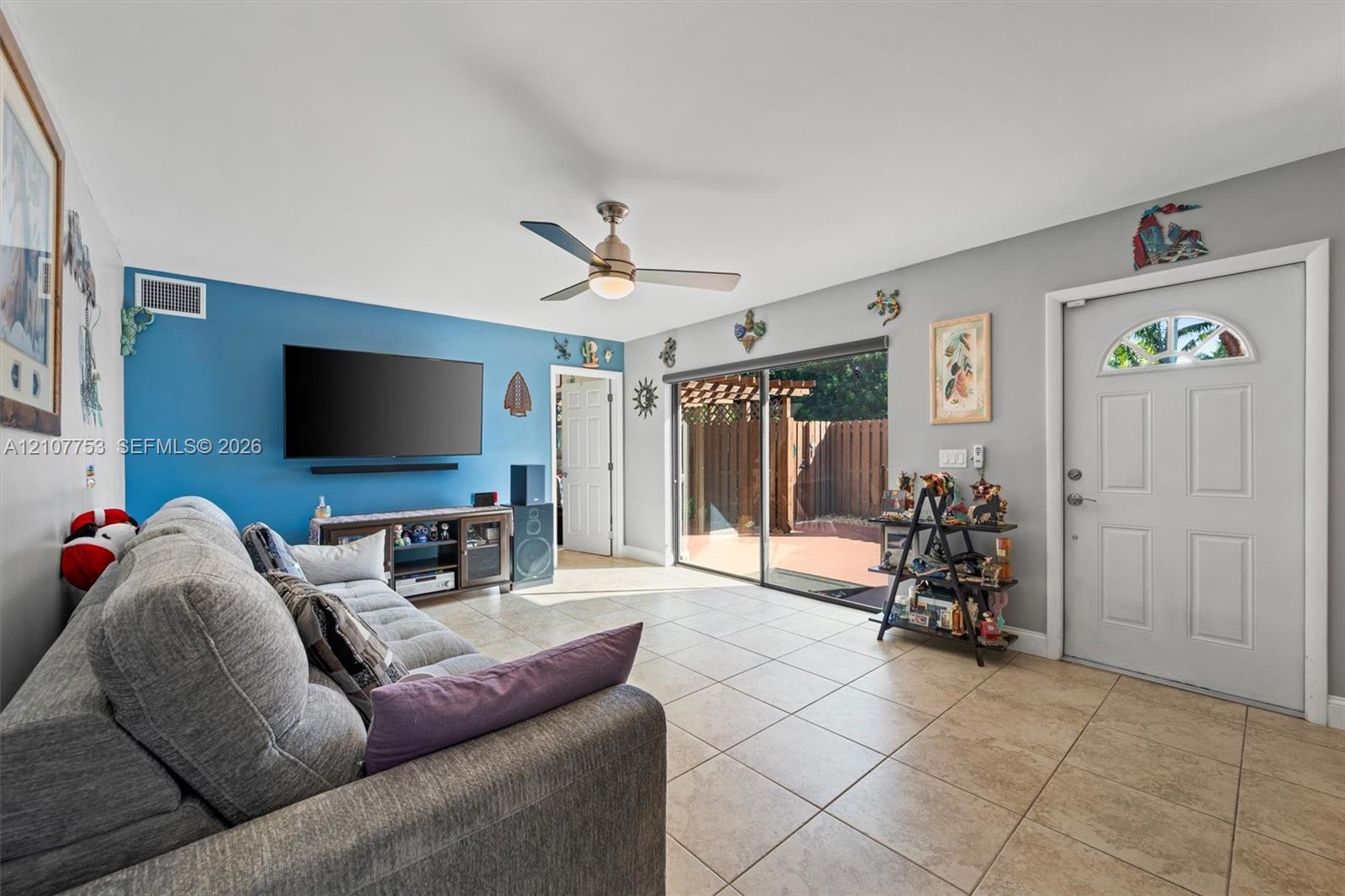 Ceramic tile flooring, sliding glass patio door, brushed metal ceiling fan with integrated lighting, and white six-panel exterior entry door with arched glass insert
