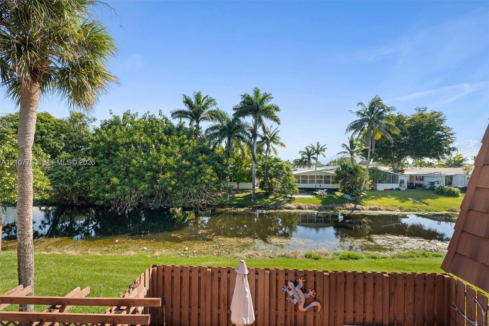 Waterfront setting featuring a wooden privacy fence, manicured lawn, and established palm trees