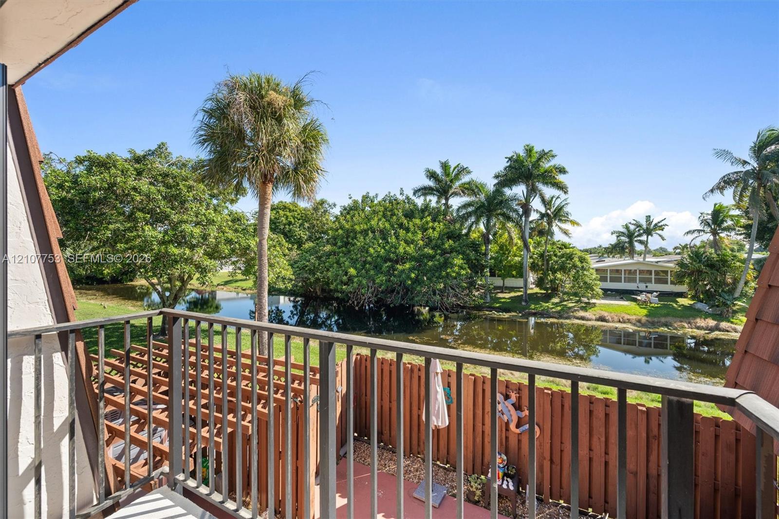 Private balcony featuring metal railings and terra cotta-toned flooring overlooking a water feature and mature palm trees