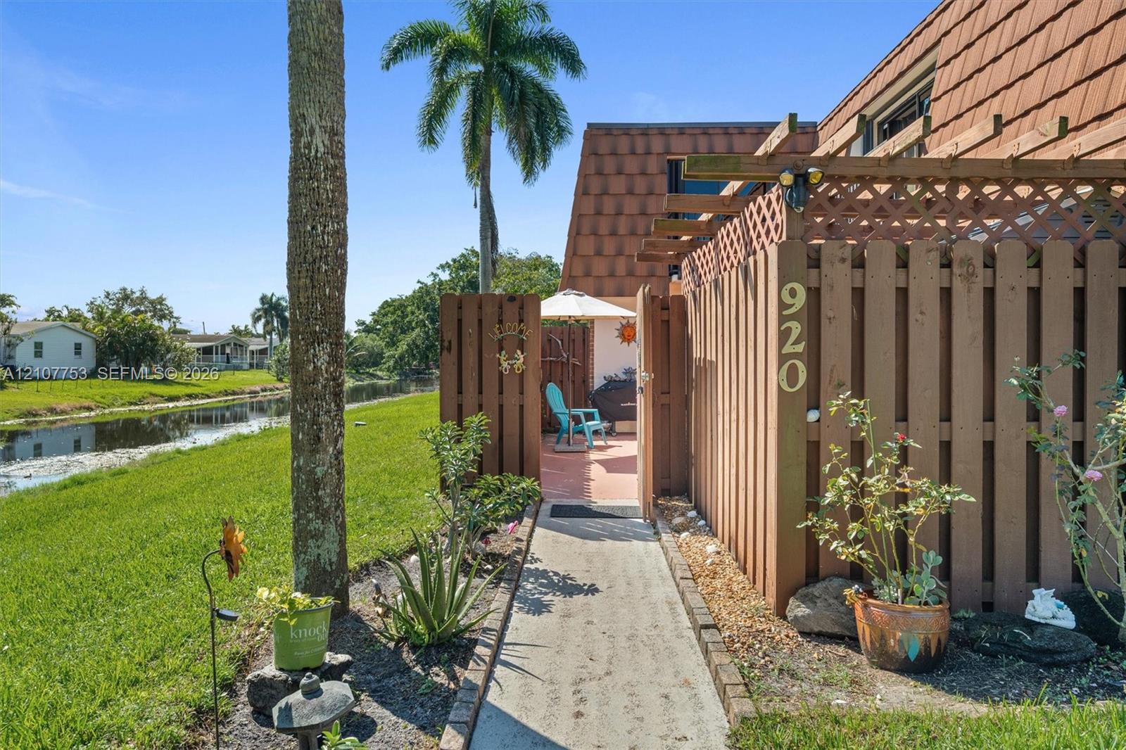 Exterior entry featuring a private wood fence, pergola, concrete walkway, and shingled roofline, situated along a waterway