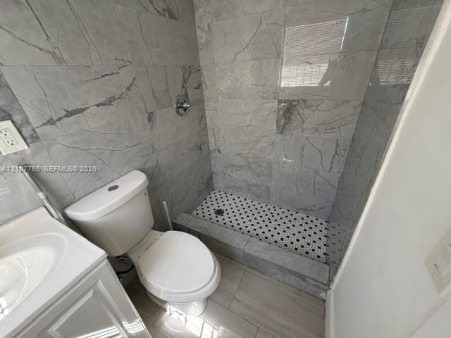 Walk-in shower with floor-to-ceiling large-format tile surround, hex-pattern mosaic floor, white vanity, and chrome fixtures
