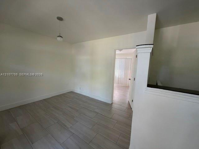 Interior space featuring wood-finish flooring, a neutral color palette, a single-bulb pendant light fixture, and a half-wall with a cap molding detail