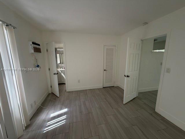Interior space featuring wood-finish tile flooring, white six-panel interior doors, a louvered closet door, and a wall-mounted climate control unit