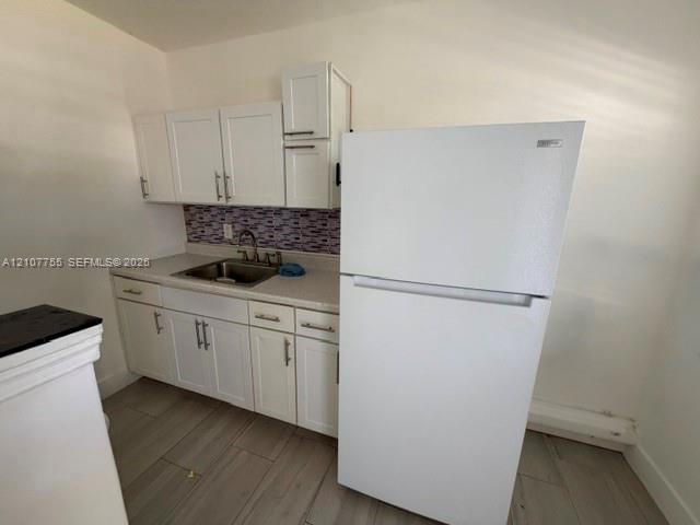 Kitchen area featuring white shaker-style cabinetry, solid-surface countertops, mosaic tile backsplash, stainless steel sink, and wood-finish flooring