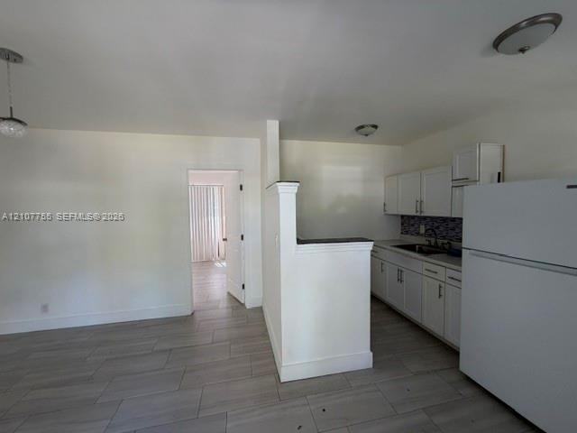 Kitchen featuring white shaker-style cabinetry, a decorative mosaic tile backsplash, solid-surface countertops, and wood-finish tile flooring throughout