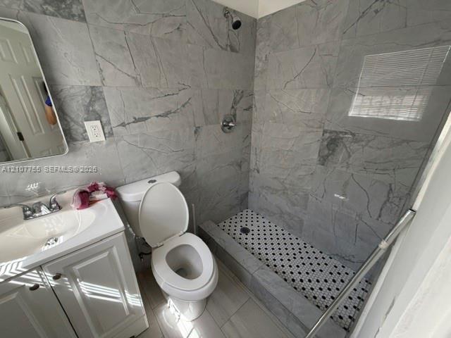 Full-height gray stone-finish wall tiling, walk-in shower with mosaic tile flooring, white vanity with integrated sink, and polished chrome fixtures