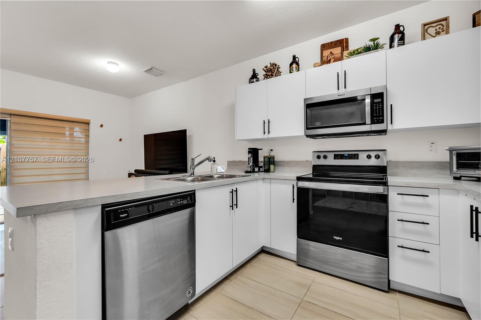 Kitchen featuring white cabinetry with matte black hardware, stainless steel appliances, a double-basin sink, and tile flooring