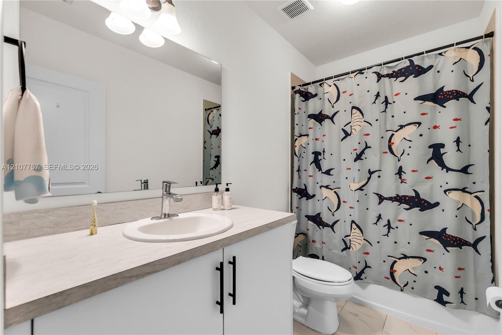 Bathroom featuring a vanity with a light-toned countertop, integrated basin, matte black hardware, a wall-to-wall mirror, and overhead track lighting