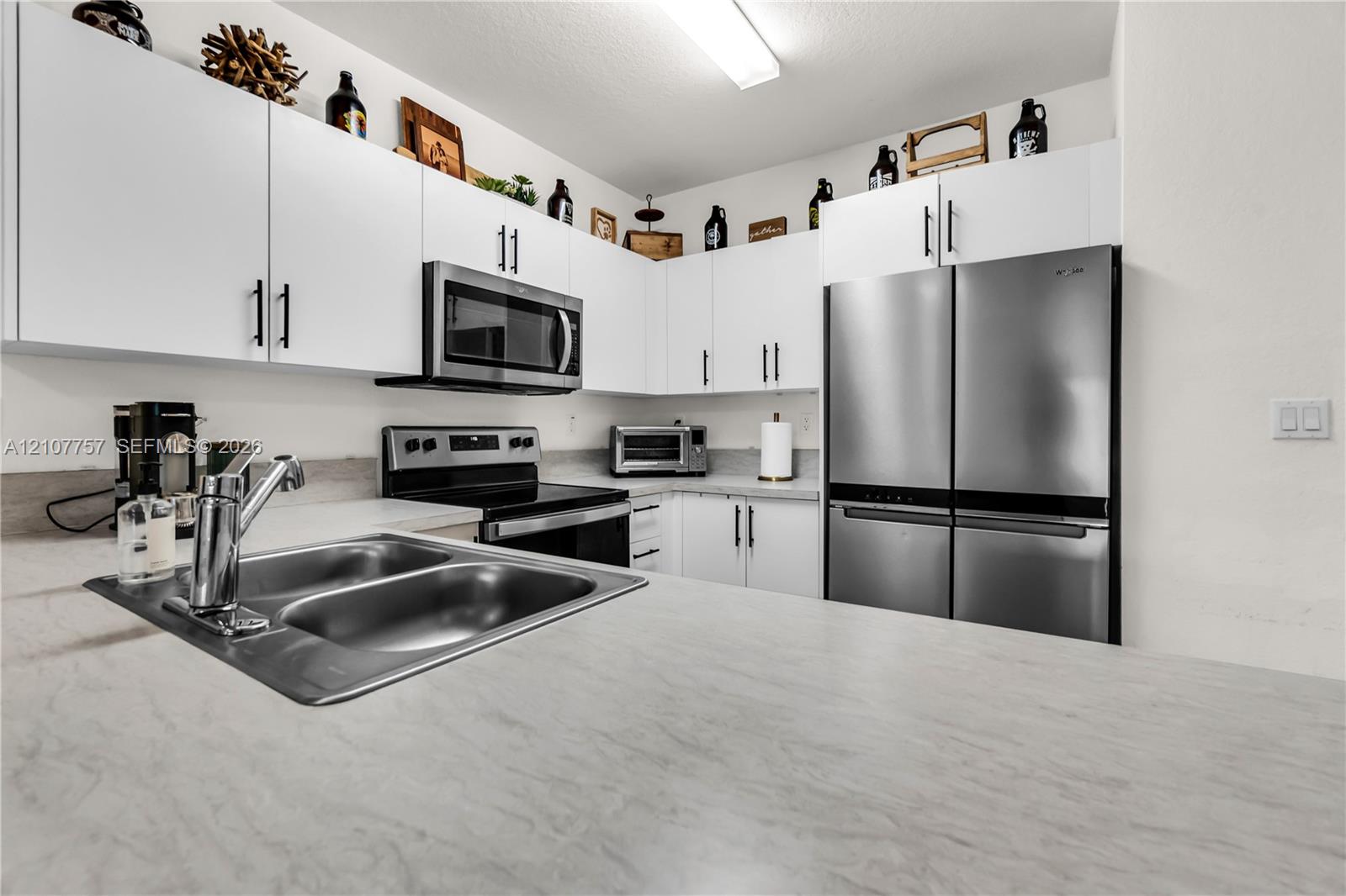 Kitchen featuring white flat-panel cabinetry, stainless steel appliances, dual-basin sink with a chrome faucet, and stone-finish countertops
