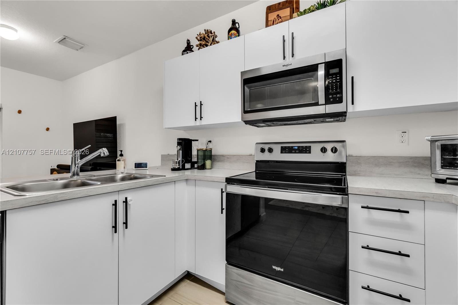 Kitchen featuring white shaker-style cabinetry, matte black hardware, stainless steel appliances, and solid-surface countertops with an integrated dual-basin sink