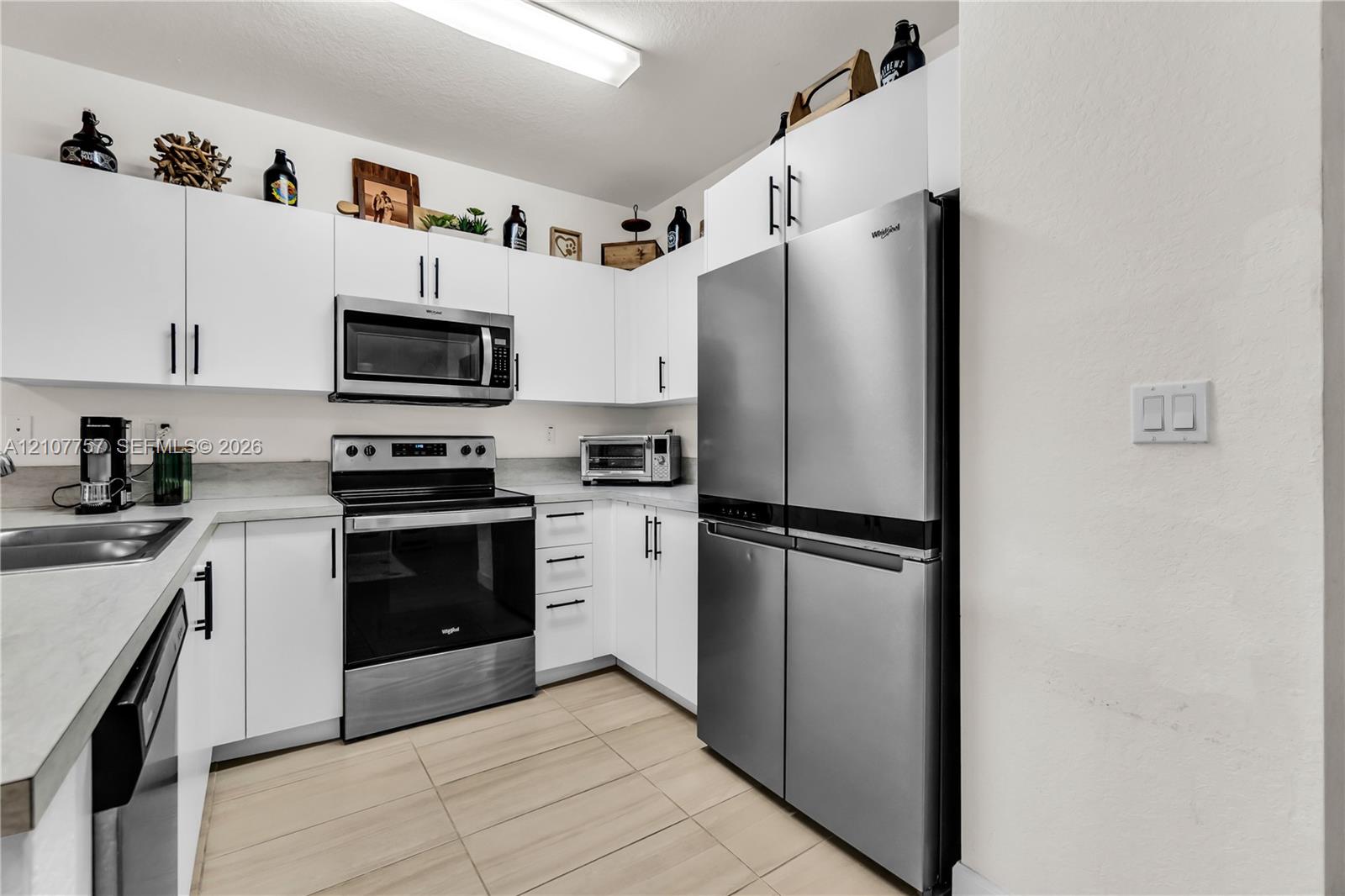 Kitchen featuring white flat-panel cabinetry, stainless steel appliances, solid surface countertops, and ceramic tile flooring