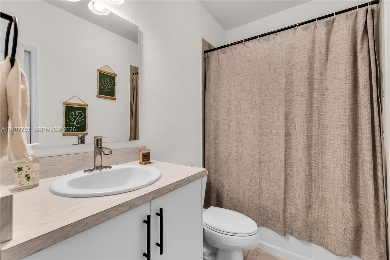 Bathroom featuring a vanity with wood-finish countertop, white cabinetry with matte black pulls, integrated oval sink, and a large wall-mounted mirror