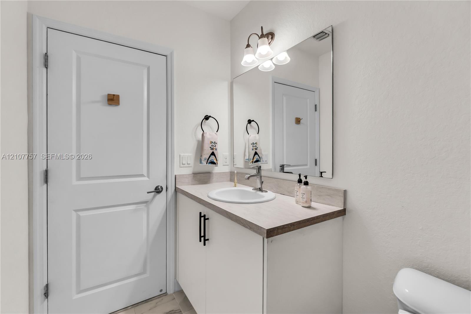 Vanity featuring a neutral-tone countertop, an integrated sink, matte black hardware, a large wall-mounted mirror, and multi-bulb decorative lighting