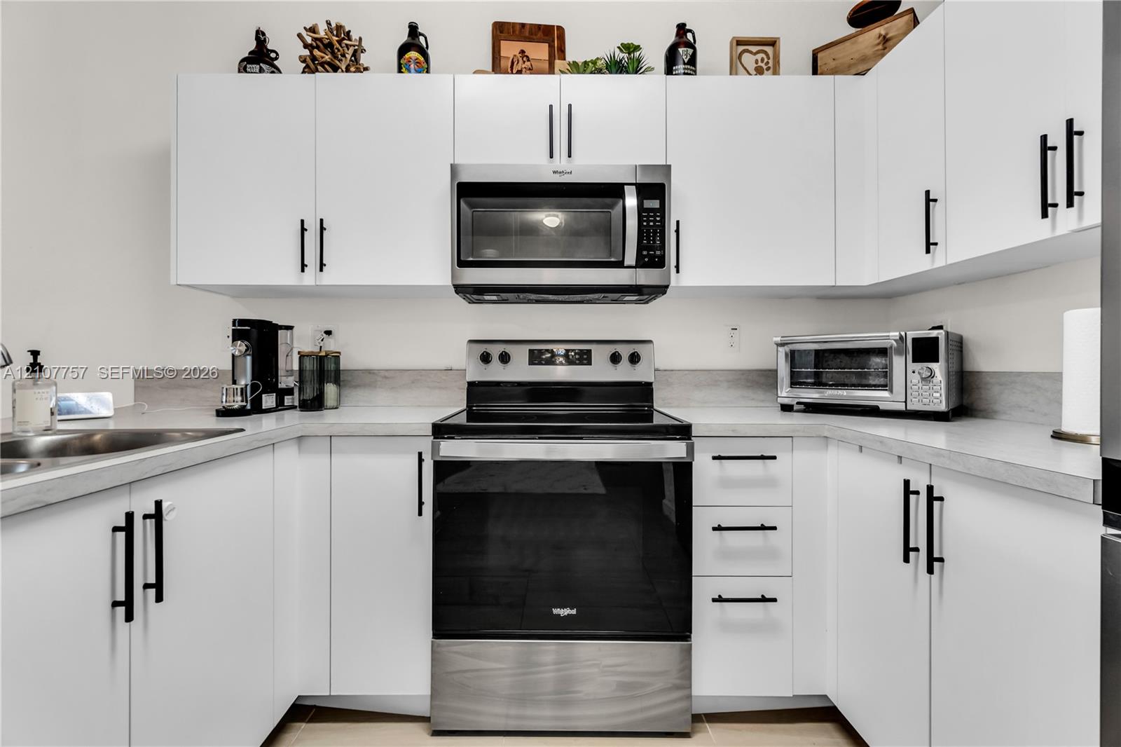 Kitchen featuring white flat-panel cabinetry, matte black hardware, stone-finish countertops, and stainless steel appliances