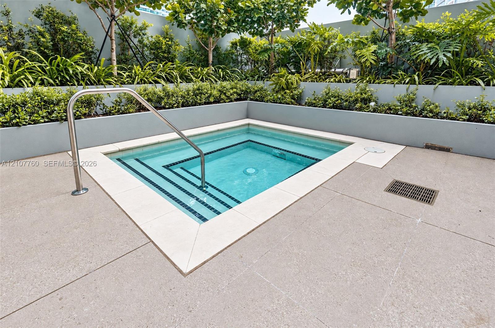 In-ground pool with integrated stepped entry and stainless steel handrail, bordered by stone-finish coping and tiered landscape planters with mature shrubbery