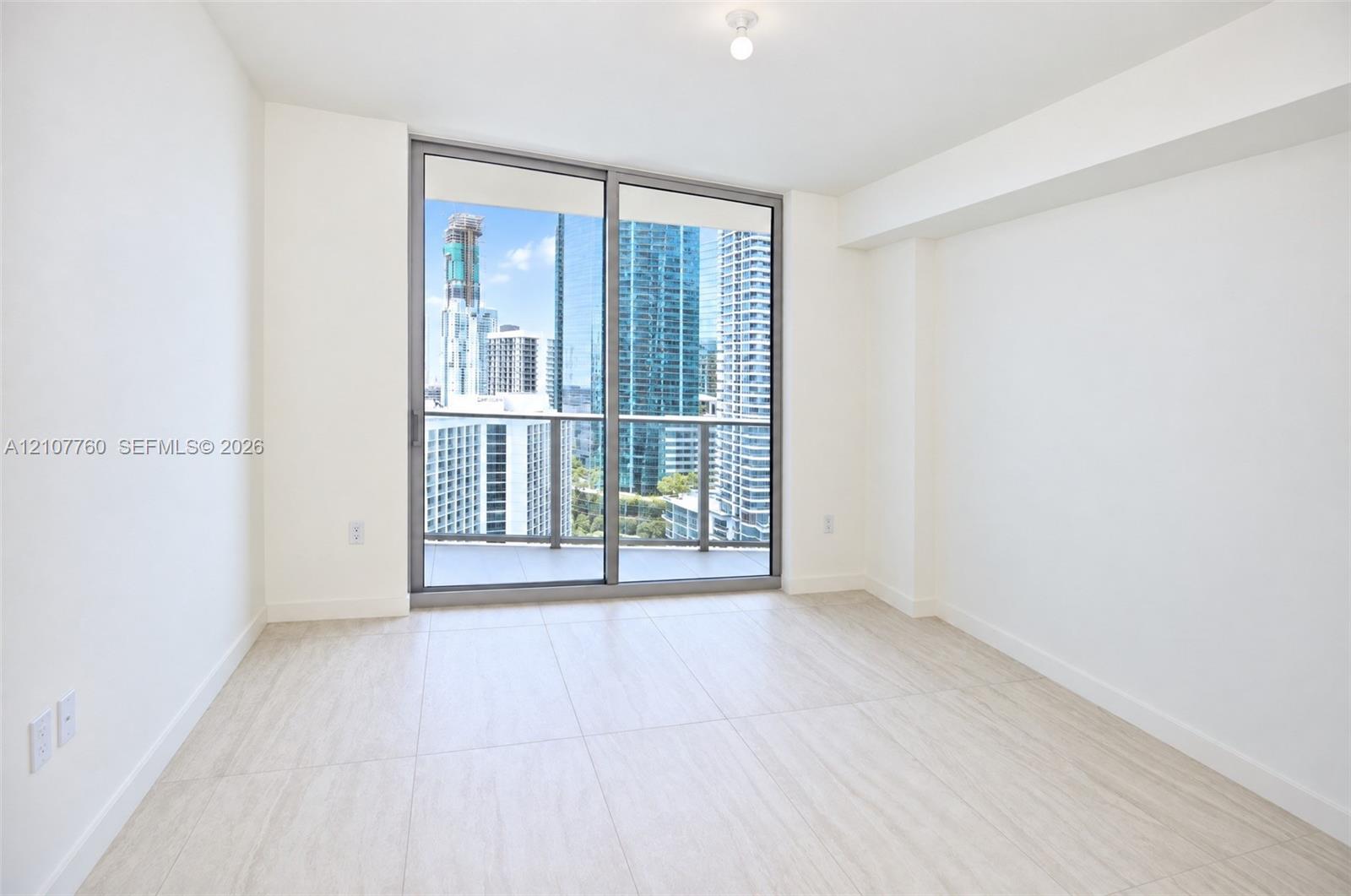 Floor-to-ceiling sliding glass doors, neutral tile flooring, and urban skyscraper scenery