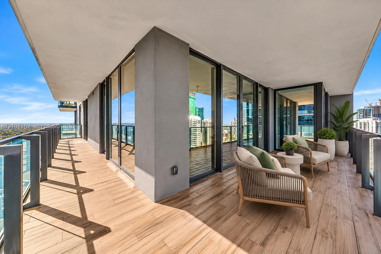 Covered wraparound balcony featuring wood-finish tile flooring, glass panel railings, and floor-to-ceiling glass doors Covered wraparound balcony featuring wood-finish tile flooring, glass panel railings, and floor-to-ceiling glass doors