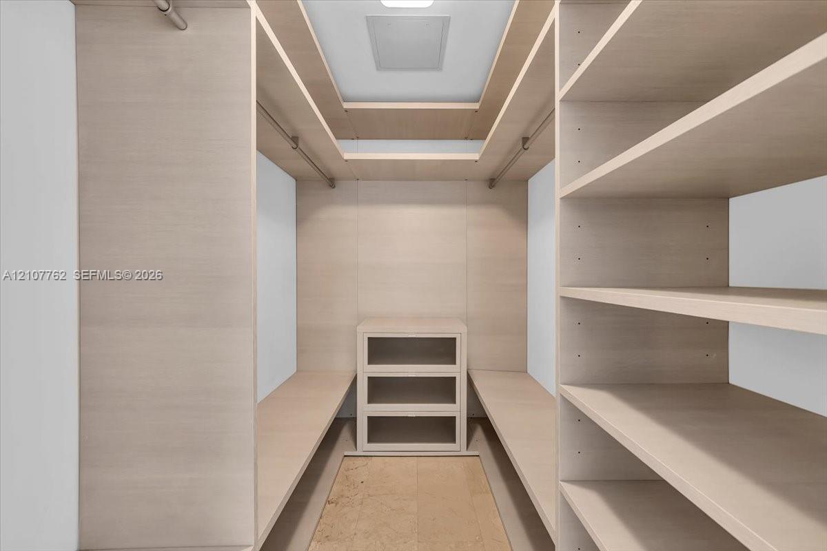 Walk-in storage featuring custom light-toned cabinetry, multi-level shelving, integrated hanging rods, and a built-in three-drawer unit