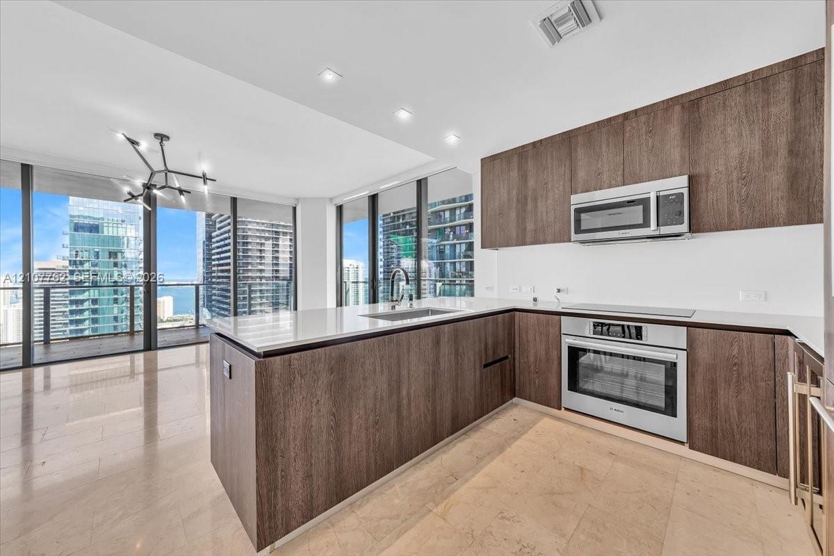 Kitchen featuring wood-finish cabinetry, stone countertops, stainless steel appliances, tile flooring, and floor-to-ceiling windows Kitchen featuring wood-finish cabinetry, stone countertops, stainless steel appliances, tile flooring, and floor-to-ceiling windows
