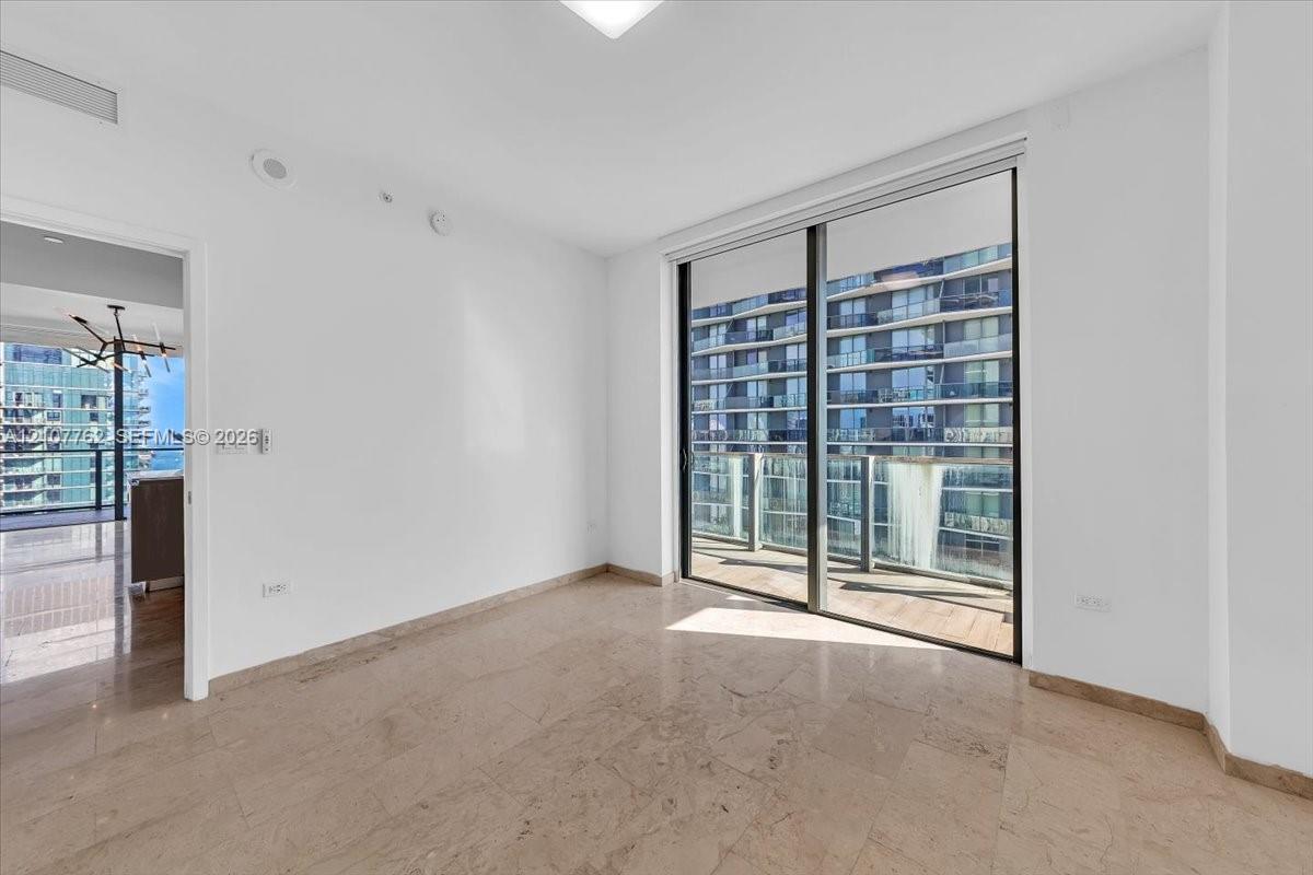Neutral stone tile flooring, floor-to-ceiling sliding glass doors, and a private balcony featuring a glass railing