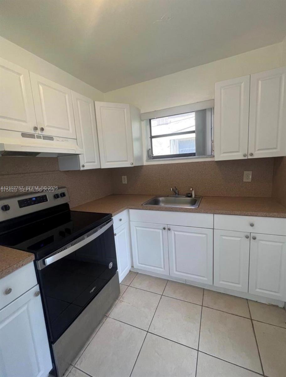 Kitchen featuring white shaker-style cabinetry, a stainless steel range, a dual-basin sink, speckled countertops, and tile flooring