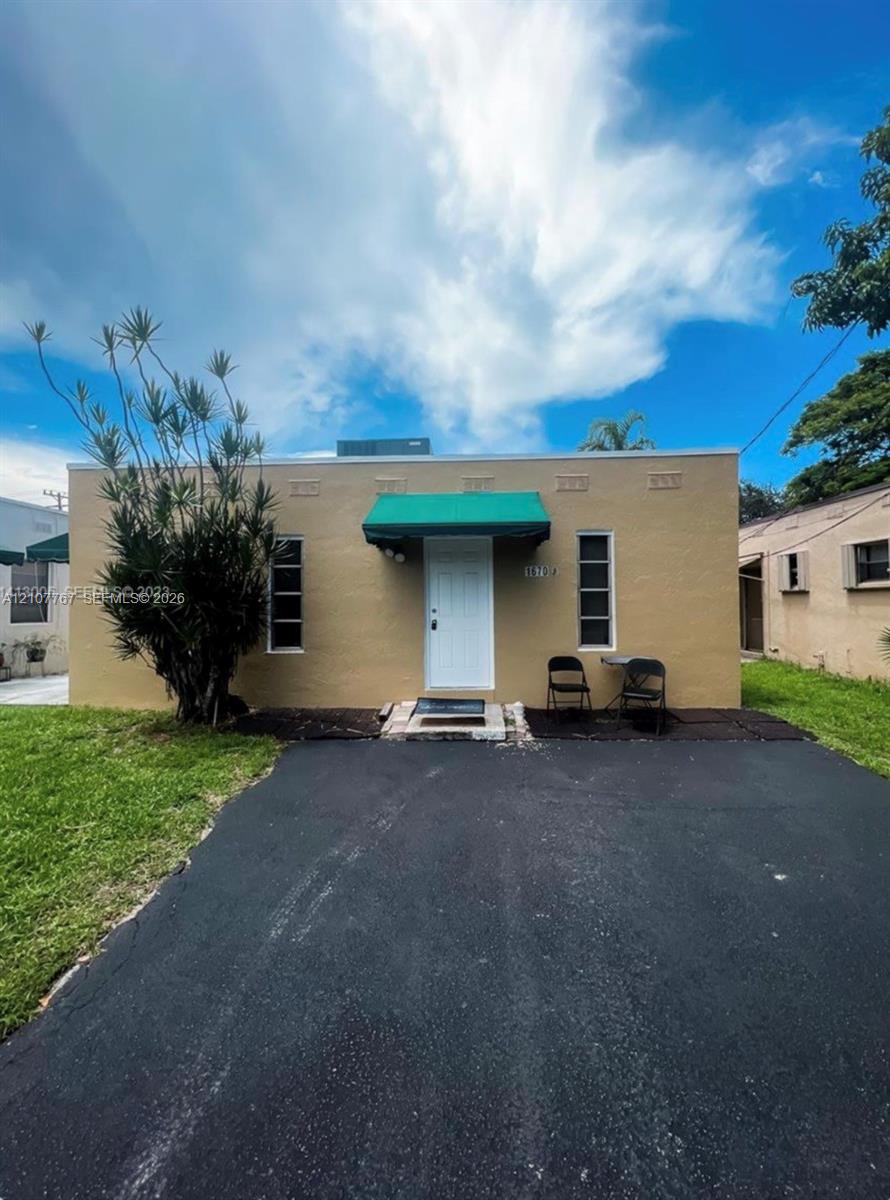 Stucco exterior featuring a paved driveway, decorative parapet wall, and green canvas awning