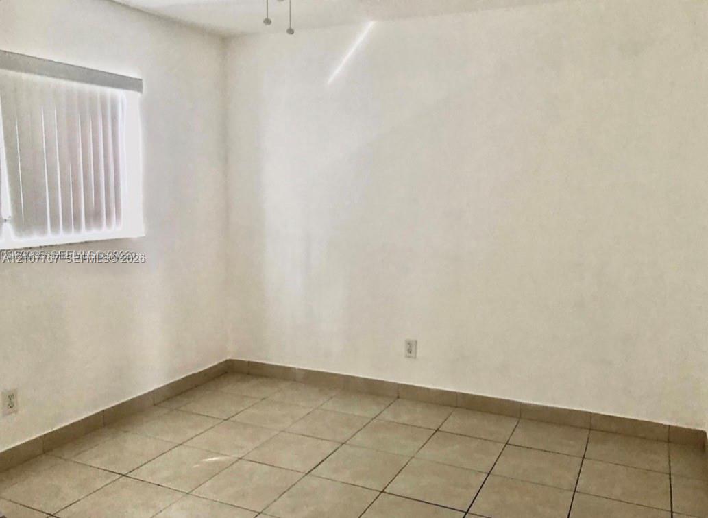 Neutral-toned interior space featuring large-format ceramic tile flooring, smooth wall finishes, and a window with vertical blinds