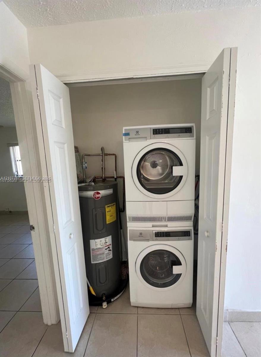 Utility closet featuring a stacked front-loading washer and dryer unit and a vertical water heater
