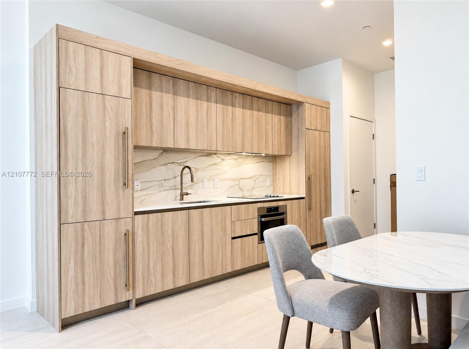 Modern kitchen featuring wood-finish cabinetry with integrated appliances, light-toned stone-style backsplash, undermount sink with a metallic pull-down faucet, and built-in cooktop and oven Modern kitchen featuring wood-finish cabinetry with integrated appliances, light-toned stone-style backsplash, undermount sink with a metallic pull-down faucet, and built-in cooktop and oven