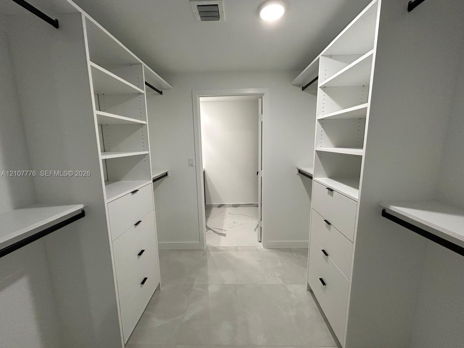 Walk-in closet featuring white built-in shelving, integrated dresser drawers with matte black hardware, and large-format tile flooring